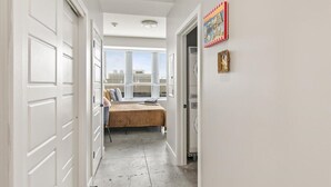 Un pasillo estrecho con puertas blancas, una cama con colcha estampada y una ventana con persianas.