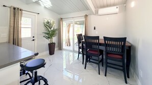 A modern kitchen with a marble countertop, a dining table with four chairs, a potted plant, and a sliding glass door leading to a patio.
