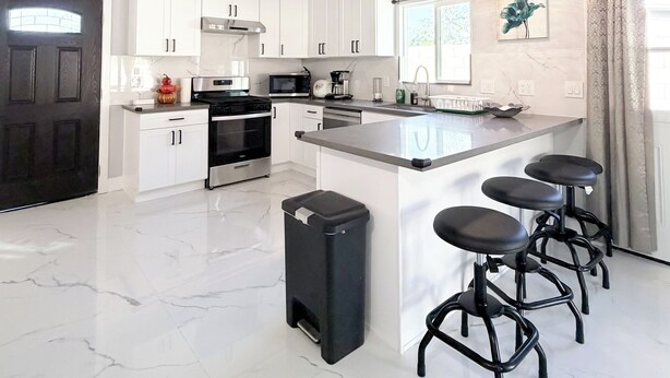 A spacious kitchen with white cabinetry, a large island with bar stools, a black trash bin, and a black door.
