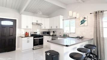 A spacious kitchen with white cabinetry, a large island with bar stools, a black trash bin, and a black door.