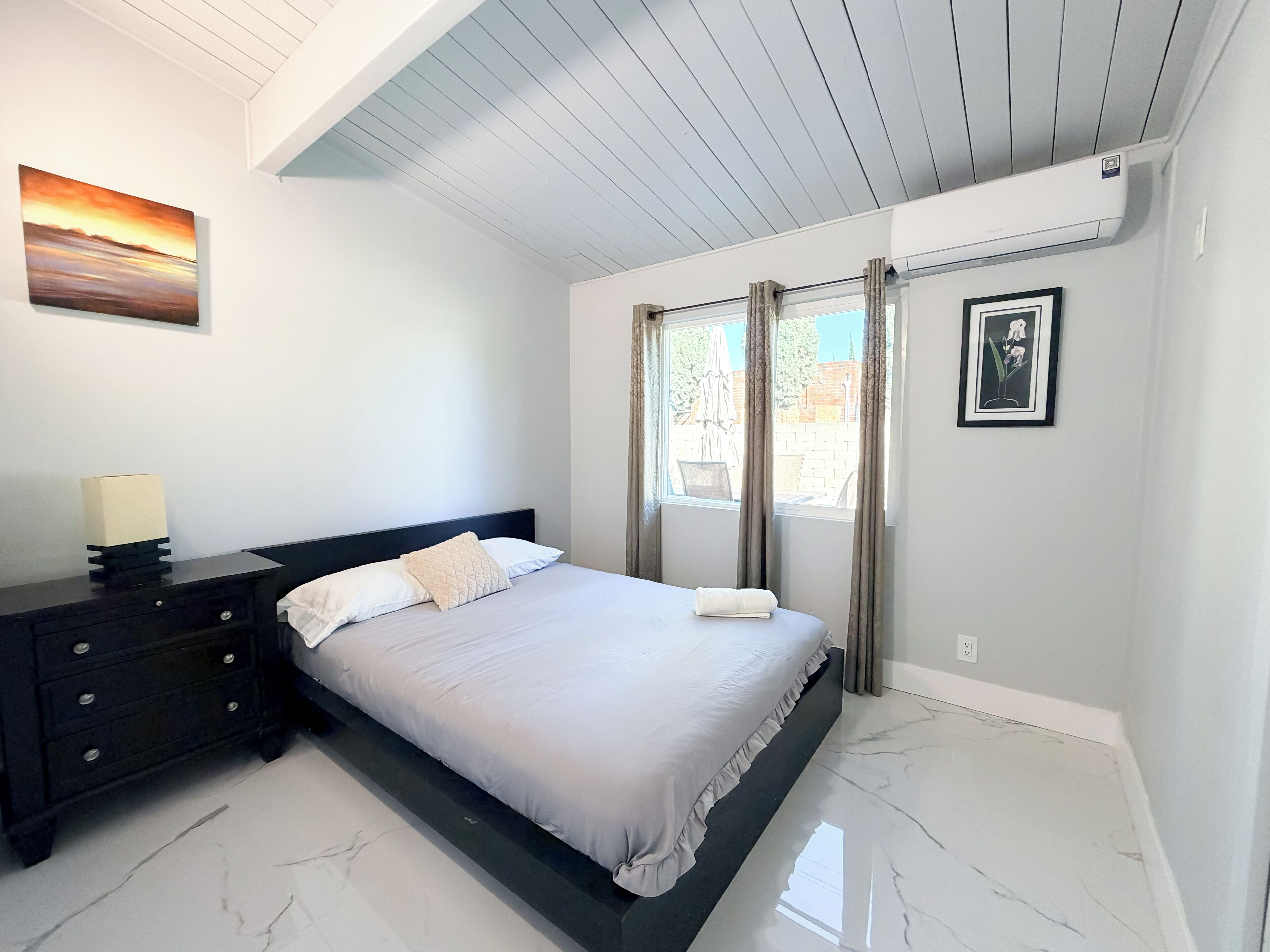 Una camera da letto con un letto, un comodino, un quadro appeso al muro e una finestra con tende.