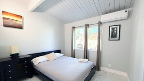 A bedroom with a bed, a nightstand, a wall-mounted painting, and a window with curtains.