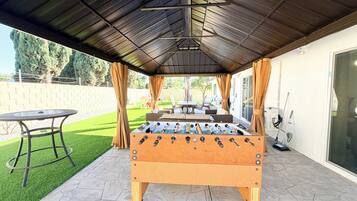 An outdoor patio area with a foosball table, a table, and chairs.
