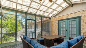 A covered patio with wicker furniture, a stone wall, and large windows. - Cherry Street Retreat - 1 Block from Main! (Bandera)