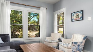 A living room with a grey sofa, two armchairs with blue floral upholstery, a wooden coffee table, and large windows with white curtains. - Cherry Street Retreat - 1 Block from Main! (Bandera)