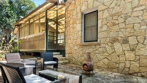 An outdoor patio with wicker furniture, a stone wall, and a wood-burning stove. - Cherry Street Retreat - 1 Block from Main! (Bandera)
