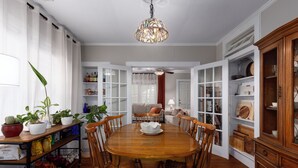 Une salle à manger avec une table et des chaises en bois, entourée d’armoires et d’étagères blanches où sont disposés divers objets.