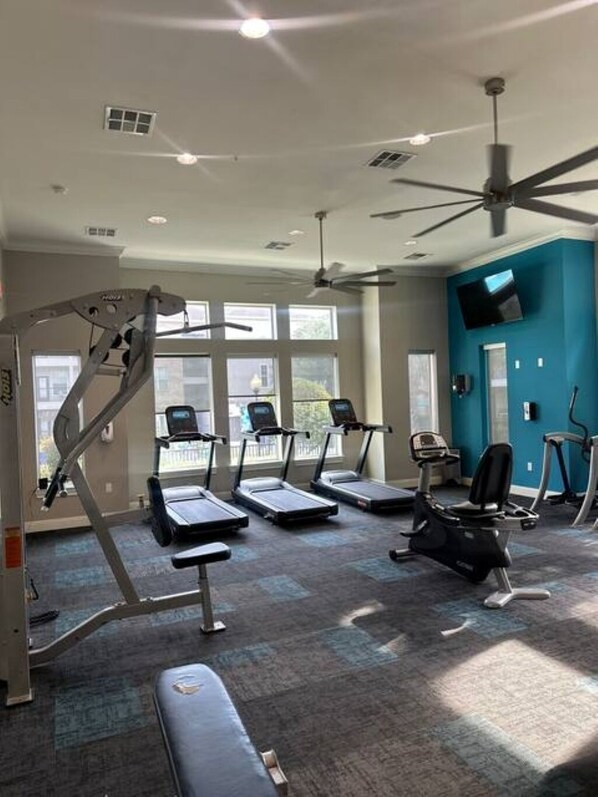 A gym with treadmills, elliptical machines, and a ceiling fan.