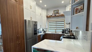 Een moderne keuken met witte kastjes, een roestvrijstalen koelkast, een marmeren aanrechtblad en twee barkrukken.