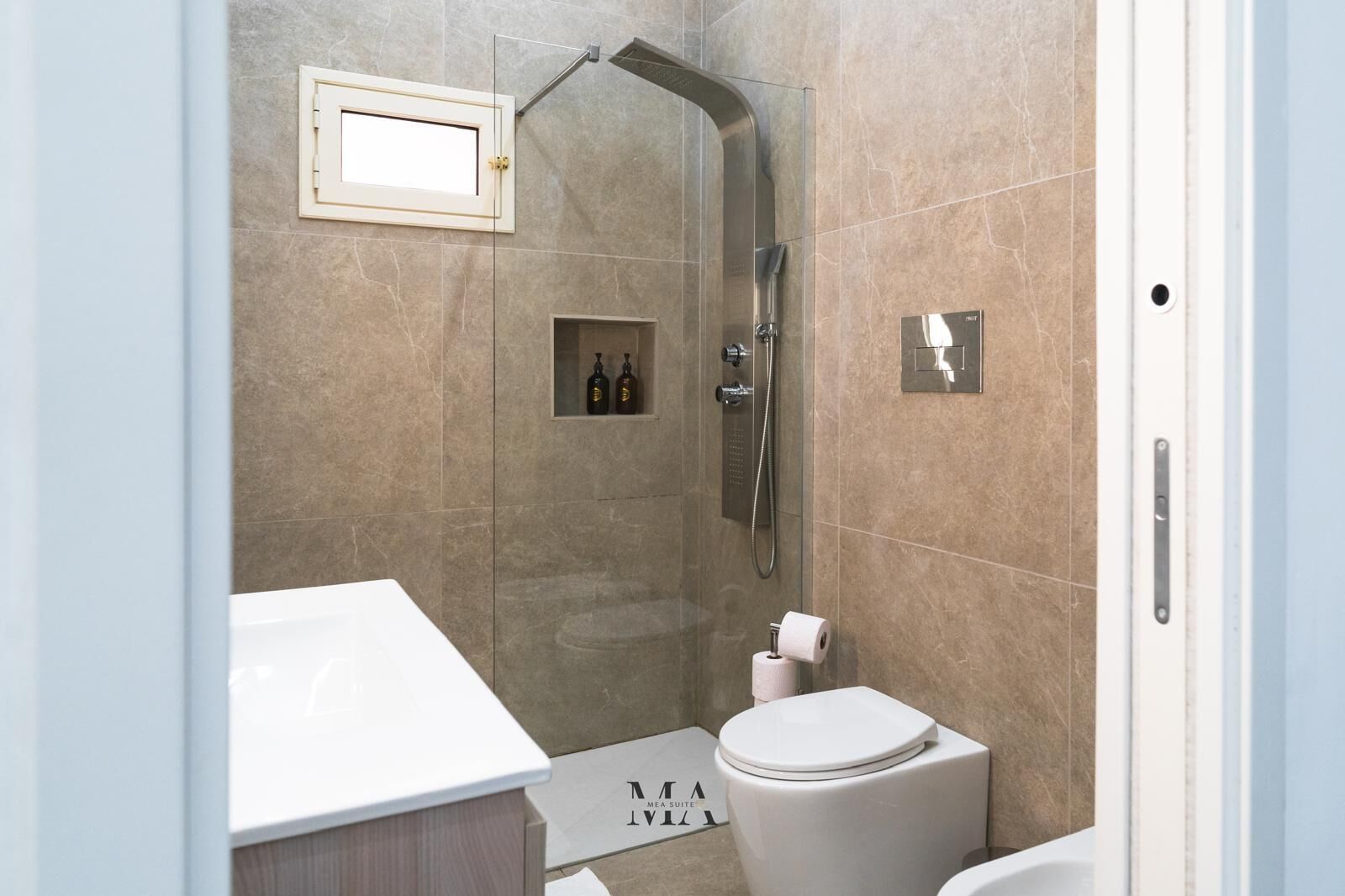 Ein modernes Badezimmer mit einer gläsernen Duschkabine, einer weißen Toilette und einem Waschtisch mit Spiegel.