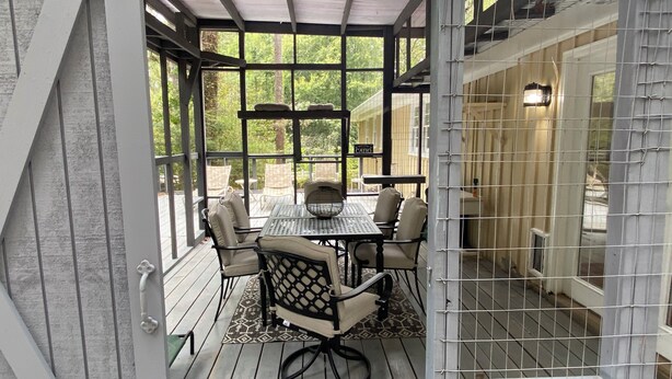 Un patio couvert avec une table et des chaises, de grandes fenêtres et une vue sur l’extérieur.