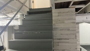 Un escalier à la finition grise et un mur recouvert de panneaux en bois.