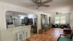 Une cuisine spacieuse dotée d’un îlot central, un coin repas avec une table verte et un salon avec un canapé et des fauteuils.