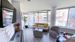 A modern living room with a sofa, coffee table, and a TV mounted on the wall. - Downtown Vancouver Condo, Pool, Gym, Skytrain (Vancouver)