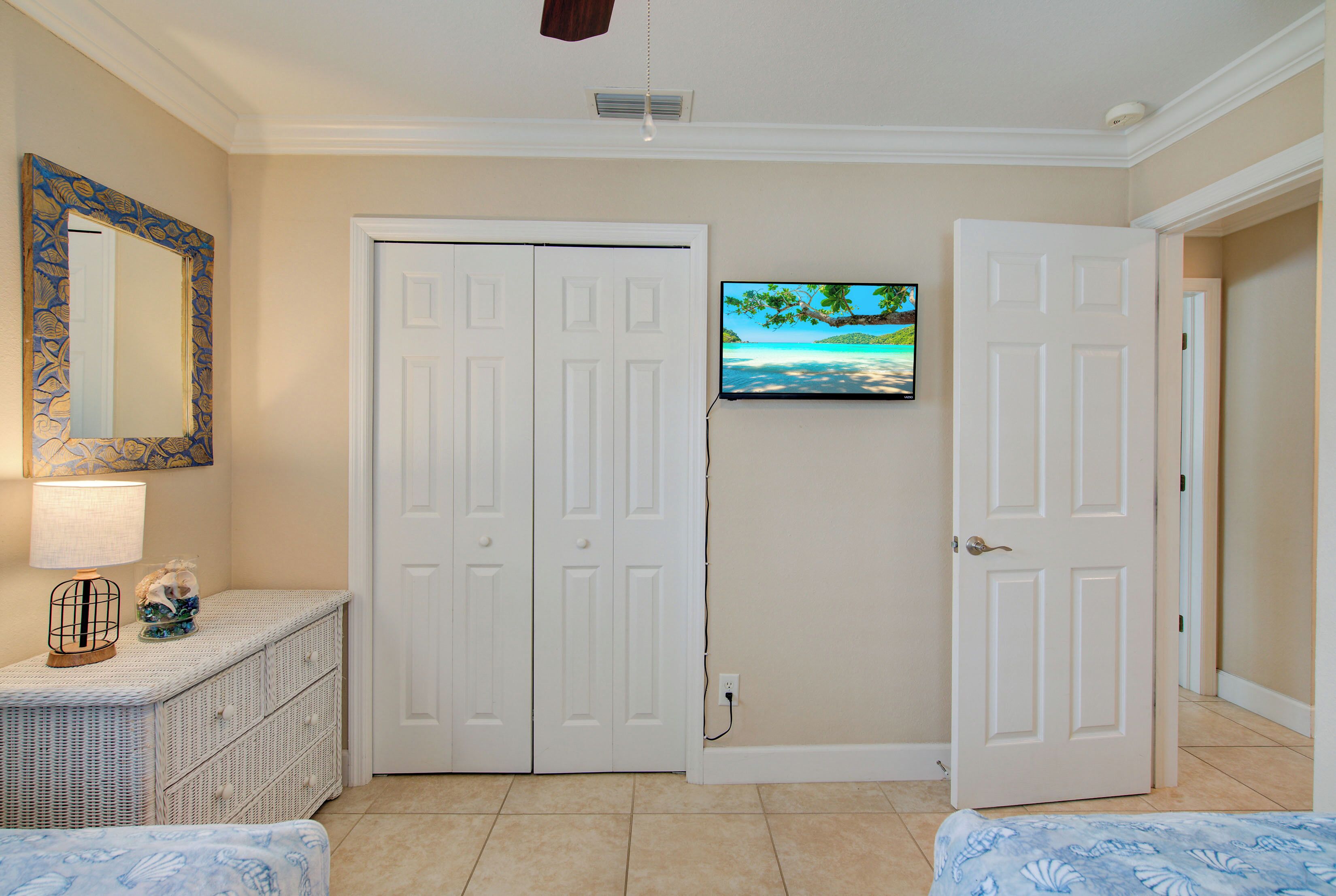 A hotel room with a bed, a dresser, a TV mounted on the wall, and a door leading to another room.