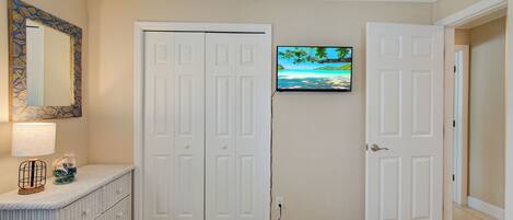 A hotel room with a bed, a dresser, a TV mounted on the wall, and a door leading to another room.