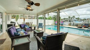 Ein überdachter Außenbereich mit Korbmöbeln, einem Deckenventilator und Blick auf einen Pool.