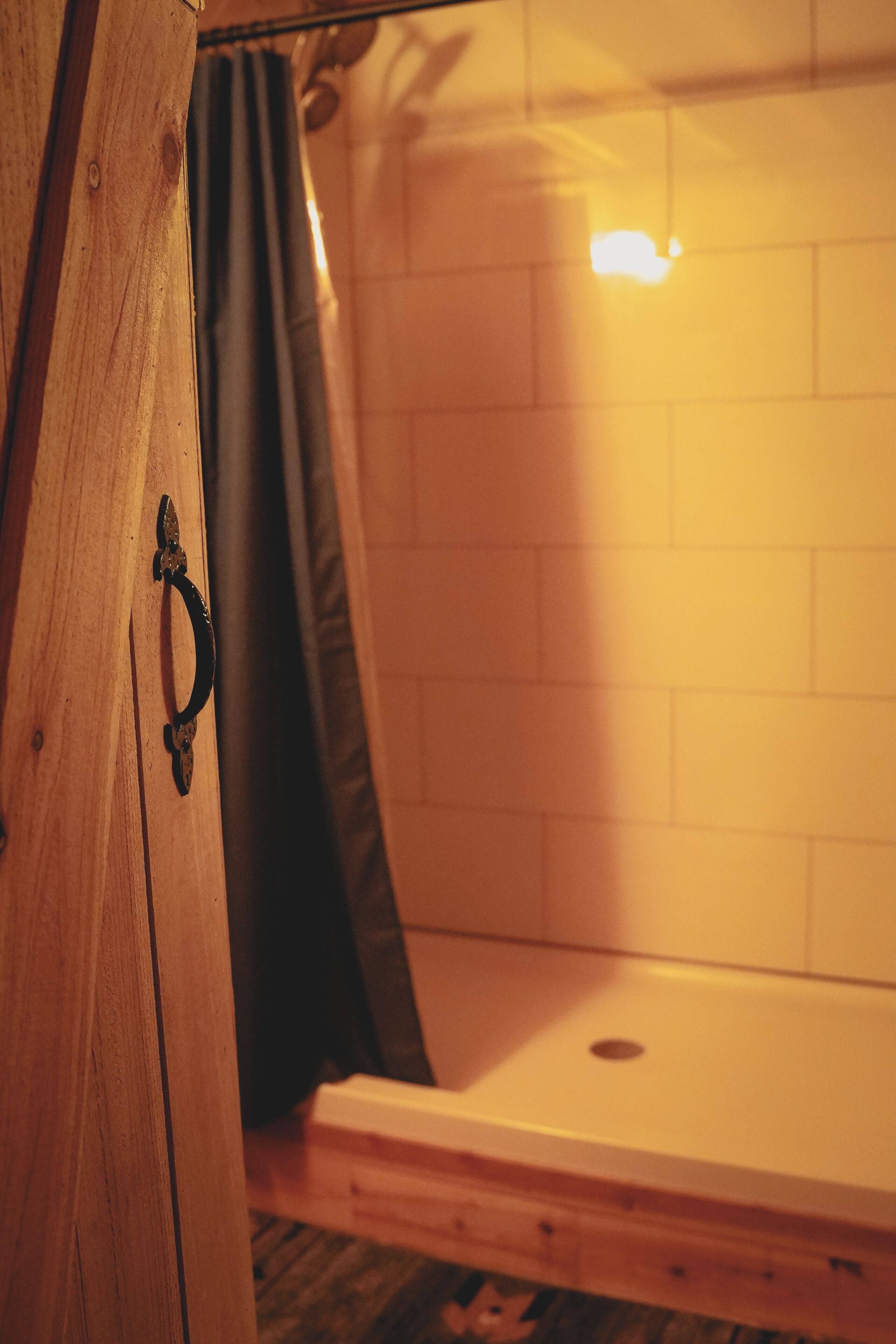 A wooden cabinet with a metal handle, a black curtain, and a white tiled wall.