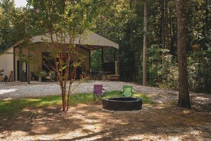 A rustic cabin with a covered porch, a fire pit, and two folding chairs.