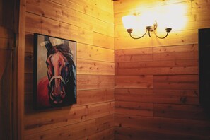 A wooden wall with a framed painting of a horse and a wall-mounted light fixture.