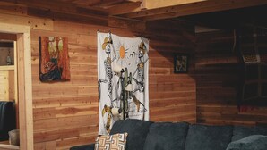 Interior acogedor de una cabaña con pared de madera, un sofá oscuro y un tapiz que representa esqueletos.