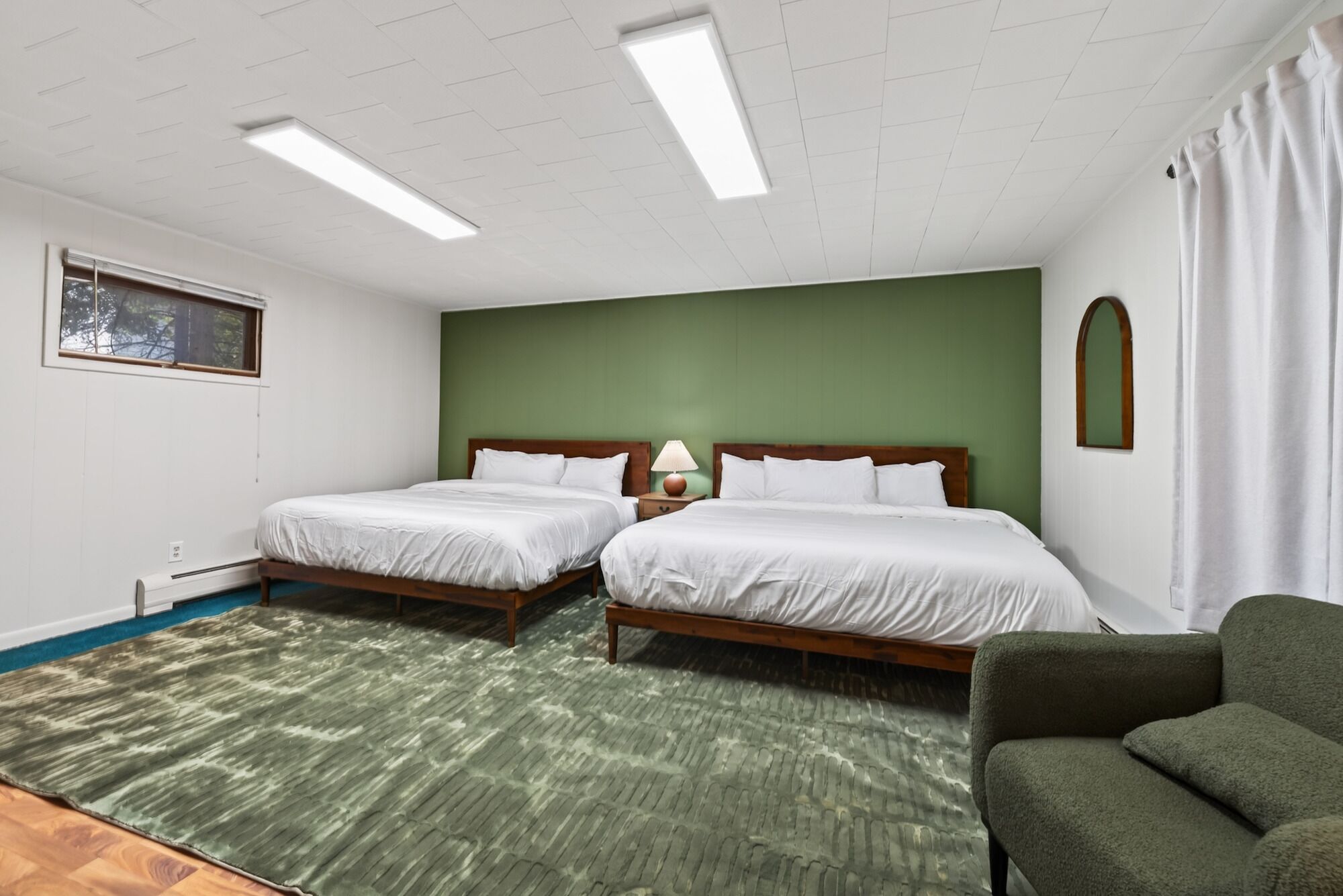 A hotel room with two beds, a green accent wall, a window, and a green sofa.
