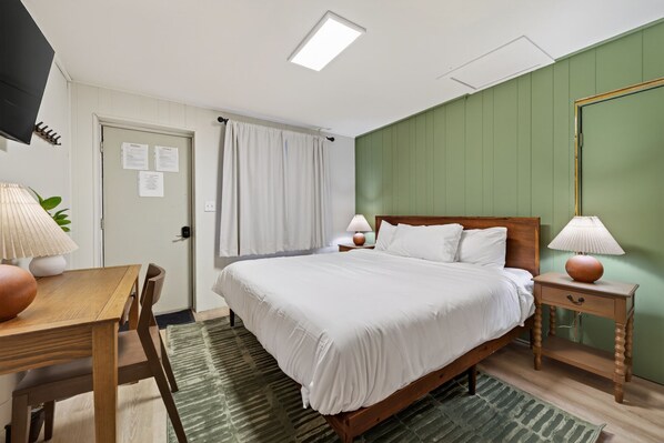 A hotel room with a bed, bedside tables, a desk, a chair, and a television.