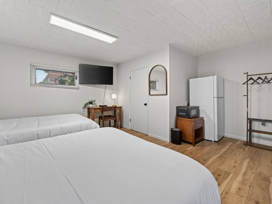 Een kamer met twee bedden, een bureau, een televisie, een spiegel, een koelkast en een kapstok.