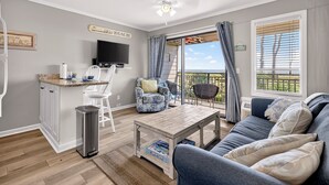Un salon comprenant un canapé, une table basse, un téléviseur et donnant sur l’extérieur.
