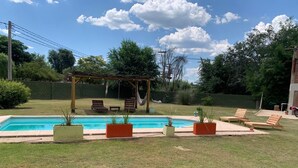 Um quintal com piscina, cadeiras de descanso e um pergolado.
