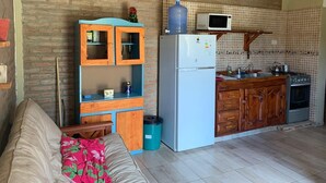 Uma cozinha compacta com geladeira, micro-ondas e fogão. Um armário de madeira com portas de vidro fica ao lado da cozinha. Um dispensador de água azul está sobre a geladeira.
