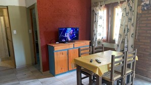 Uma área de refeições com mesa e cadeiras de madeira, uma televisão sobre um móvel de madeira e uma parede vermelha.