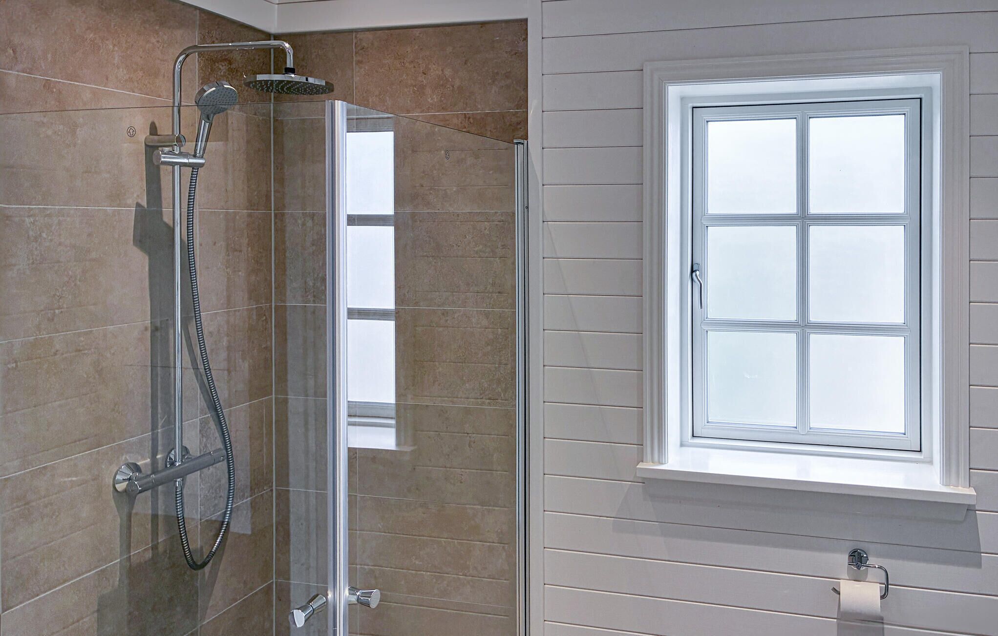A bathroom with a glass-enclosed shower, a white window with six panes, and a towel rack below the window.