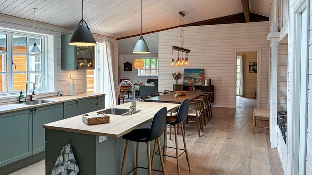 A kitchen with a central island, bar stools, pendant lighting, and a dining area with a long table.