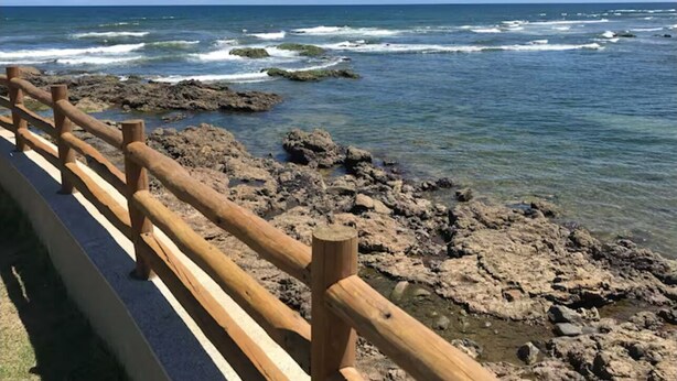 A wooden railing along a rocky shoreline with clear blue water and a calm sea. - Apartment in Salvador in the best location. (Salvador)