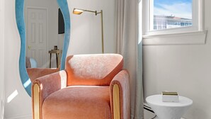 A room with a large mirror, a pink chair, a floor lamp, a small round table, and a window with a view of a building. - Prof Cleaned | Linens+Towels | Fast WIFI | Coffee (Lake Como)