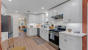 A modern kitchen with white cabinets, a stainless steel stove, and a dining area with a bench. - Prof Cleaned | Linens+Towels | Fast WIFI | Coffee (Lake Como)