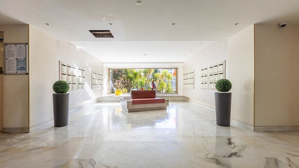 A spacious lobby with a marble floor, a central red bench, and potted plants. - Wonderful Apartment Croisette Martinez - Parking (Cannes)