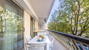 A balcony with a dining table and chairs, a view of trees, and a car parked outside. - Wonderful Apartment Croisette Martinez - Parking (Cannes)