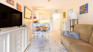 A living room with a sofa, TV, dining table, and chairs. There is a kitchen in the background with cabinets and a clock. - Wonderful Apartment Croisette Martinez - Parking (Cannes)