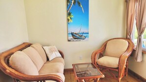 A room with a wicker sofa, a matching armchair, and a glass coffee table. - Utila Seabreeze Vacation Apartments (Isla de Utila)