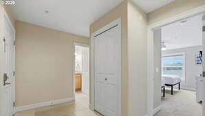 Un corridoio con pareti beige, una porta bianca e una camera da letto con un letto e una finestra.