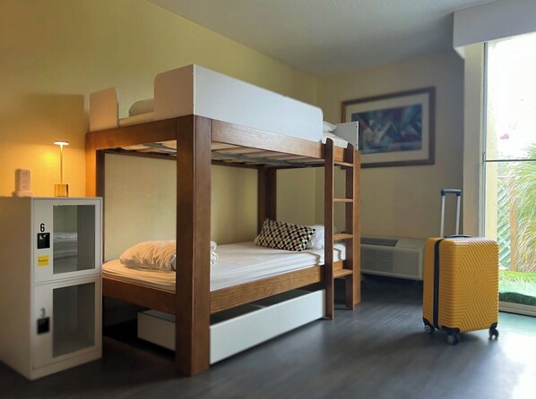 A bunk bed room with a desk, a suitcase, and a window with a view of greenery. - Bposhtels Waikiki Retreat (Honolulu)