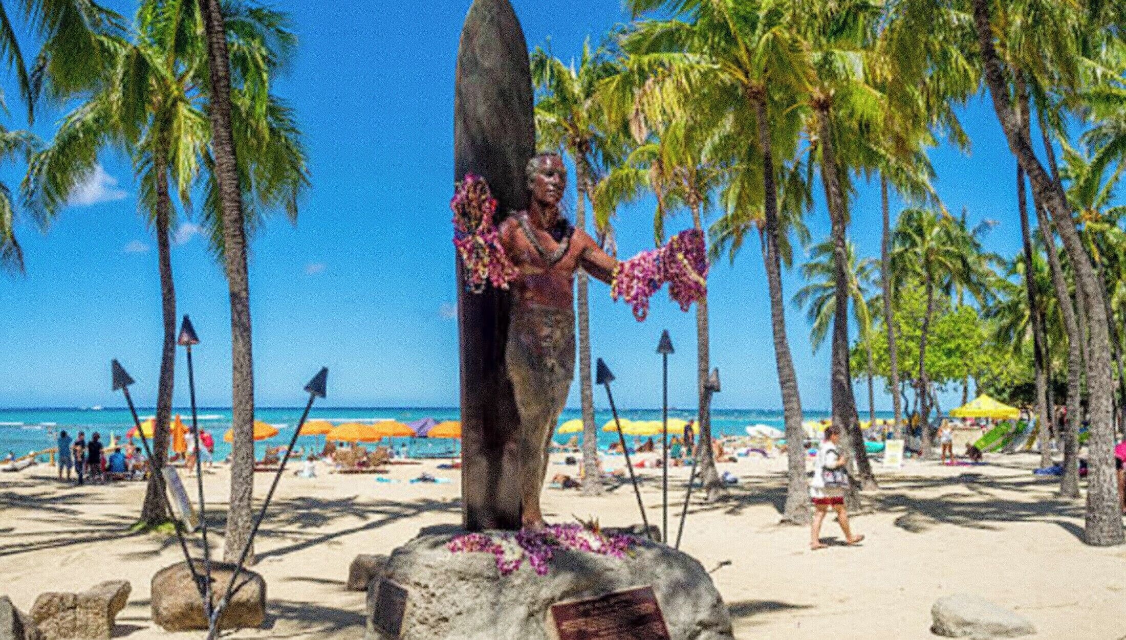 A beach scene with a large stone monument, palm trees, and beach umbrellas.