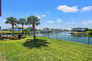 A waterfront property with a grassy area, palm trees, and a view of a body of water. - 4BR Waterfront • Boat Slip + Kayaks • Sunsets (Hernando Beach)