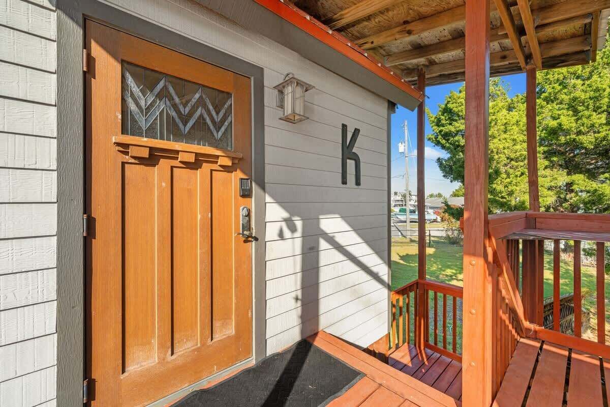 Une porte en bois ornée d’un motif géométrique, une lettre « K » peinte sur le mur et une véranda en bois avec une balustrade.