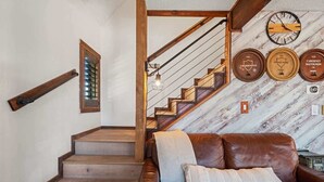 Una escalera con escalones y barandilla de madera, un sofá de cuero marrón con cojines, y una pared decorada con relojes de temática vinícola.