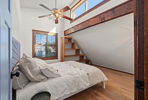 A bedroom with a bed, a ceiling fan, a window, and a wooden staircase. - 4BR Waterfront • Boat Slip + Kayaks • Sunsets (Hernando Beach)