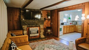 Una sala de estar con chimenea de piedra, paredes de madera, televisor y sofá.