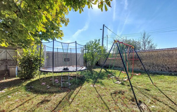 Patio trasero con trampolín, columpio y pared de piedra.